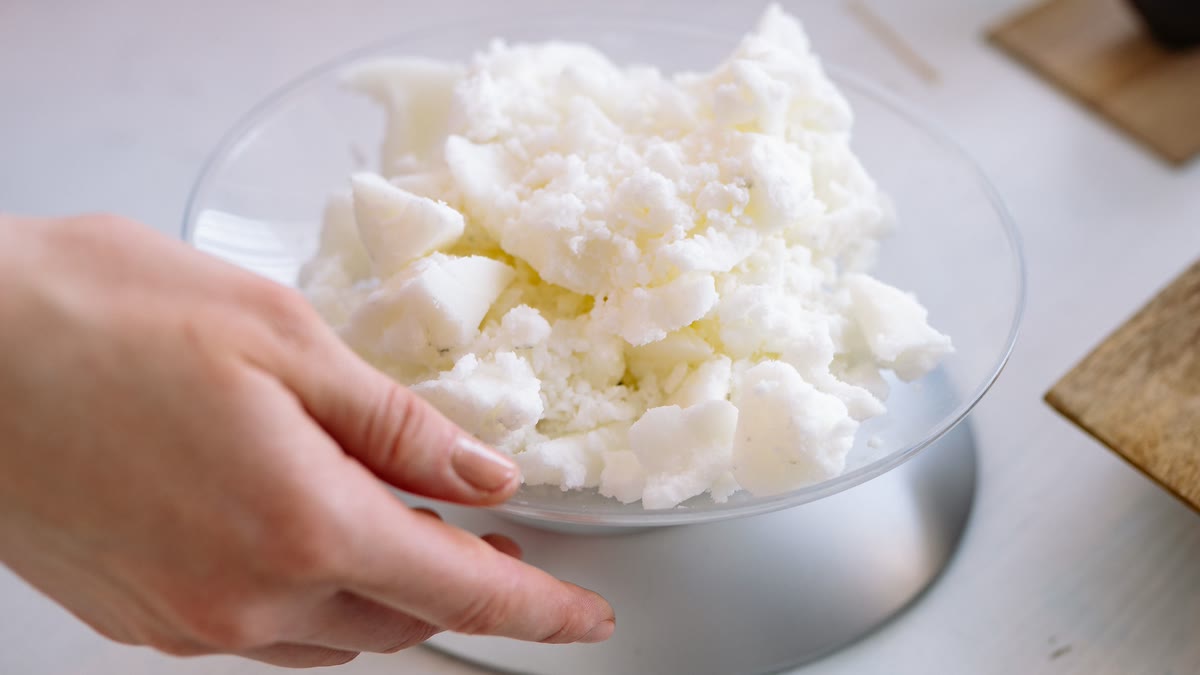 A bowl of raw shea butter pieces being weighed on a kitchen scale